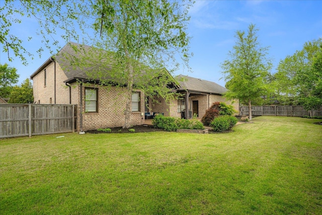 rear view of property featuring a yard, brick siding, and a fenced backyard