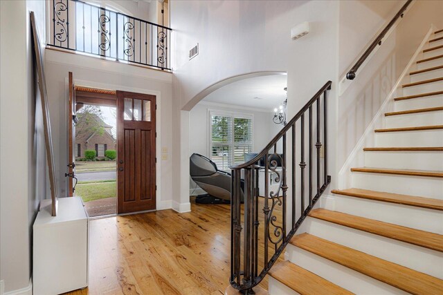 foyer entrance featuring stairway, light wood-style floors, visible vents, and arched walkways