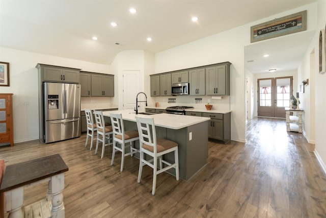 kitchen featuring a kitchen breakfast bar, dark wood-style flooring, stainless steel appliances, and an island with sink