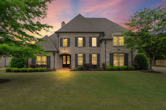 french provincial home featuring a chimney, roof with shingles, a front yard, french doors, and brick siding