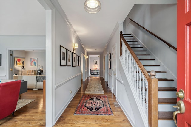 hall with ornamental molding, visible vents, stairway, and wood finished floors