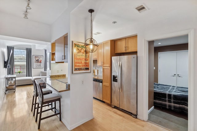 kitchen featuring visible vents, a kitchen bar, light wood-type flooring, decorative light fixtures, and stainless steel appliances