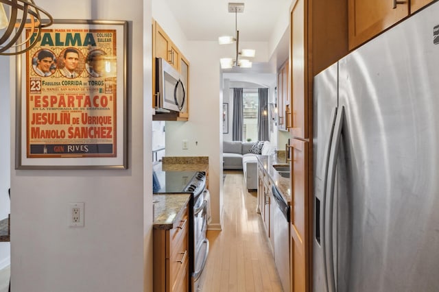 kitchen featuring light stone countertops, appliances with stainless steel finishes, light wood-style floors, brown cabinetry, and decorative light fixtures