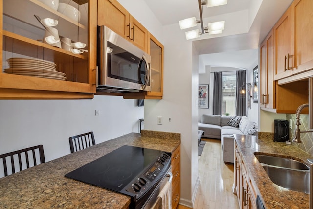 kitchen with a sink, light wood finished floors, electric stove, stainless steel microwave, and glass insert cabinets