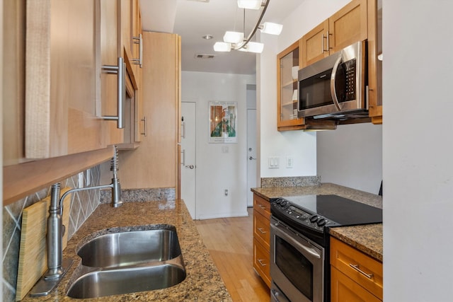kitchen featuring brown cabinetry, visible vents, light wood-style floors, dark stone countertops, and stainless steel appliances
