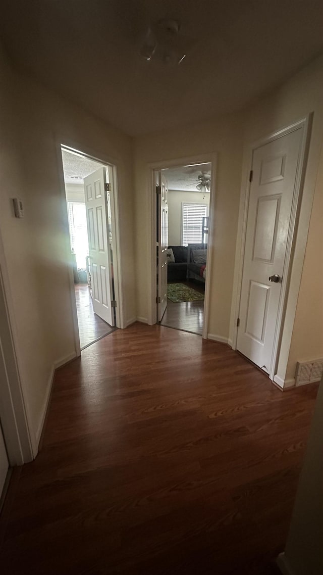 corridor with dark wood-style floors, visible vents, and baseboards