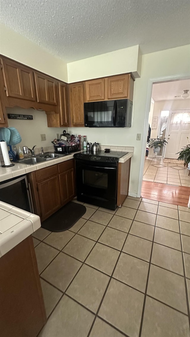 kitchen with a sink, light tile patterned floors, black appliances, tile countertops, and a textured ceiling