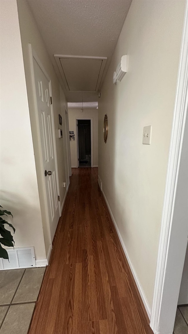 corridor with attic access, visible vents, baseboards, a textured ceiling, and wood finished floors