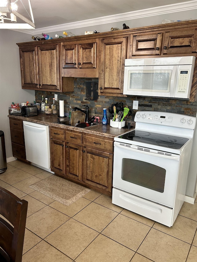 kitchen featuring light tile patterned floors, crown molding, a sink, dark countertops, and white appliances