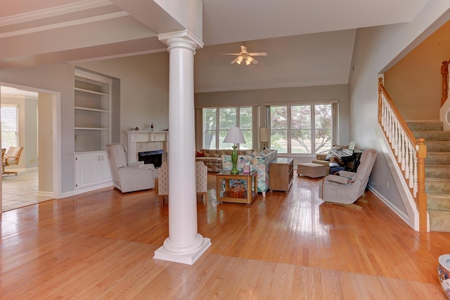 living room featuring ornate columns, ceiling fan, light wood-type flooring, and stairway
