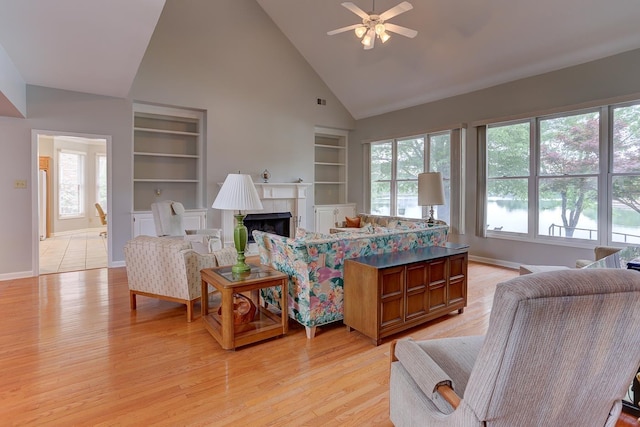 living room featuring built in shelves, high vaulted ceiling, ceiling fan, and plenty of natural light