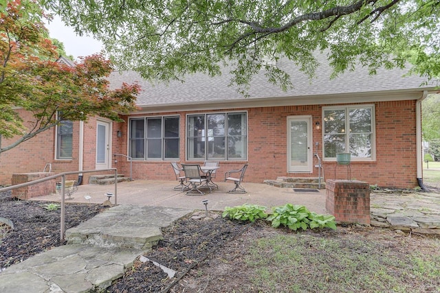 rear view of property with brick siding, roof with shingles, entry steps, and a patio area