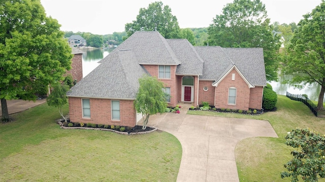 traditional home with brick siding, a water view, roof with shingles, a front lawn, and concrete driveway