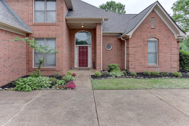 property entrance with a shingled roof and brick siding