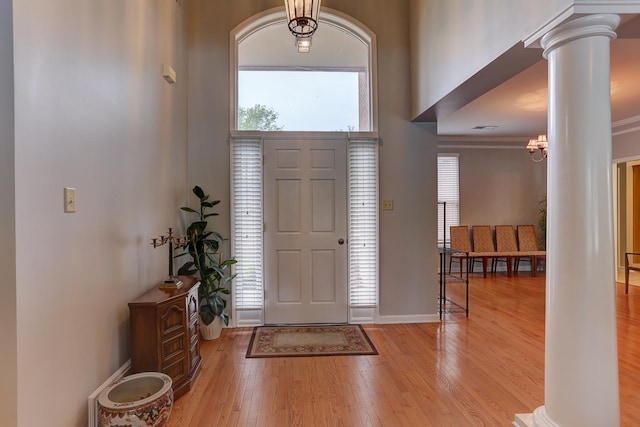 entryway with ornate columns, wood finished floors, a towering ceiling, and baseboards