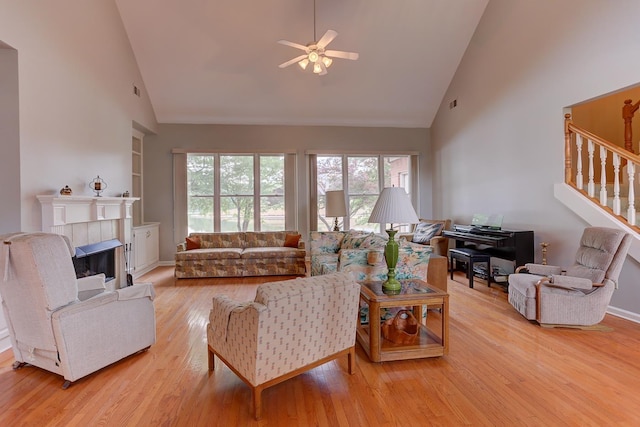 living area with stairs, light wood finished floors, a ceiling fan, high vaulted ceiling, and built in shelves
