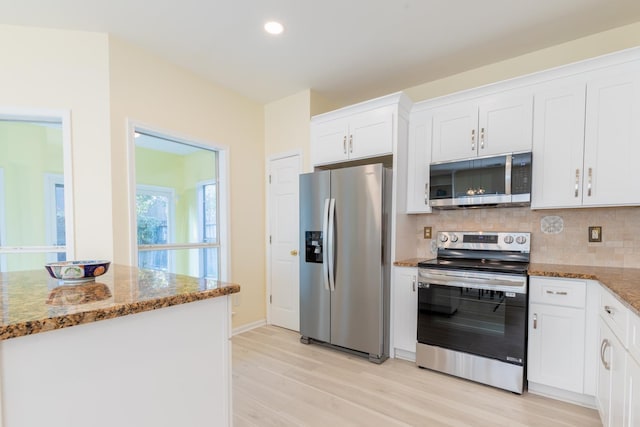 kitchen featuring dark stone countertops, stainless steel appliances, backsplash, white cabinetry, and light wood-type flooring