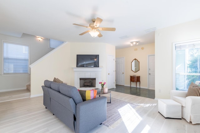 living area with stairs, a fireplace, light wood finished floors, baseboards, and a ceiling fan
