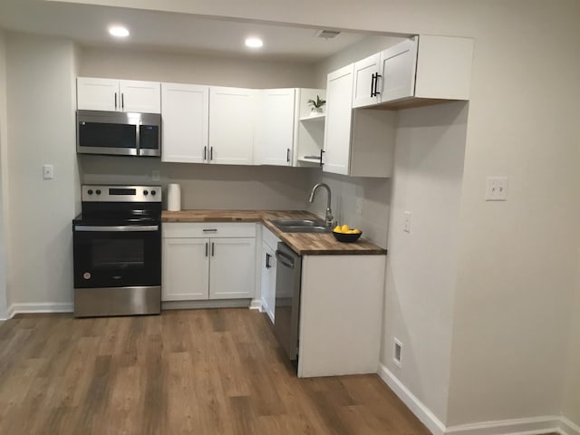 kitchen featuring wood counters, white cabinetry, light wood-style flooring, a sink, and appliances with stainless steel finishes
