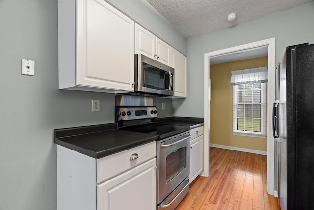 kitchen featuring white cabinetry, stainless steel appliances, dark countertops, and light wood-style floors