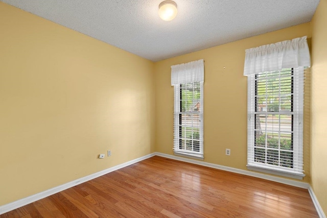 spare room featuring light wood finished floors, a textured ceiling, and baseboards