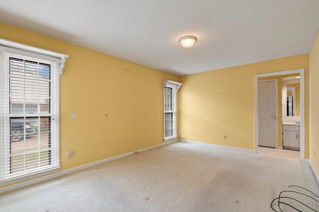 spare room featuring a textured ceiling, light colored carpet, and baseboards