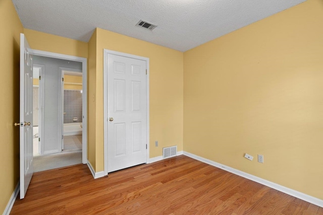 unfurnished bedroom with a textured ceiling, visible vents, light wood-style flooring, and baseboards
