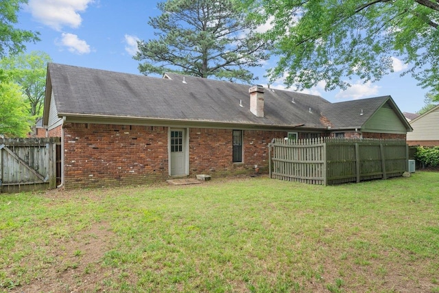 rear view of property featuring fence, a chimney, a yard, and brick siding