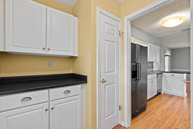 kitchen featuring stainless steel dishwasher, dark countertops, light wood-style flooring, and black fridge