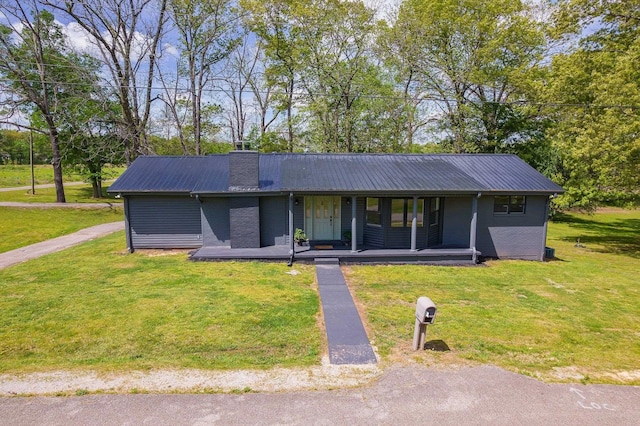 ranch-style home with covered porch, metal roof, a front yard, and a chimney
