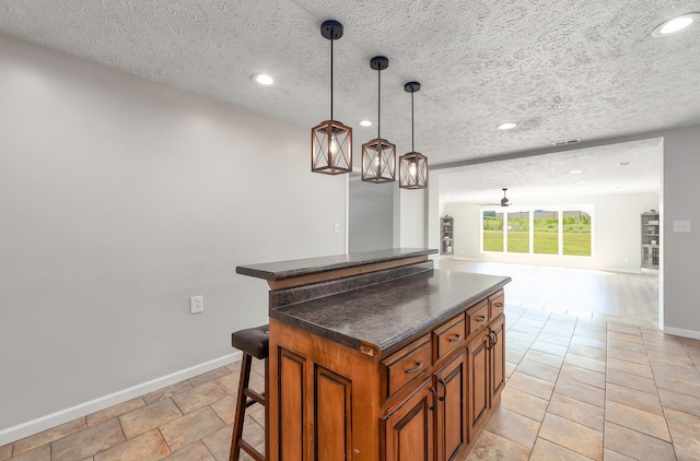kitchen with dark countertops, a kitchen breakfast bar, brown cabinets, and baseboards