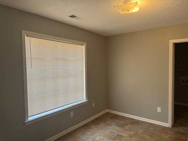 empty room featuring a textured ceiling, visible vents, and baseboards