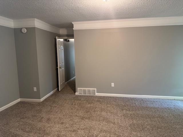 empty room featuring visible vents, carpet, baseboards, ornamental molding, and a textured ceiling