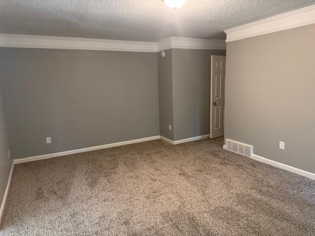 carpeted spare room featuring a textured ceiling, visible vents, crown molding, and baseboards