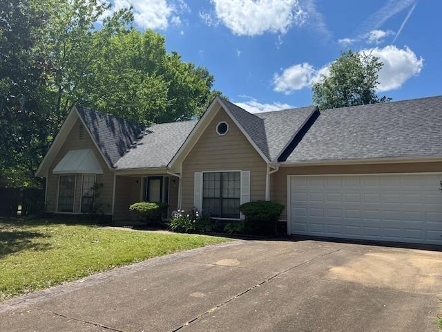 ranch-style home with a garage, a front lawn, driveway, and roof with shingles
