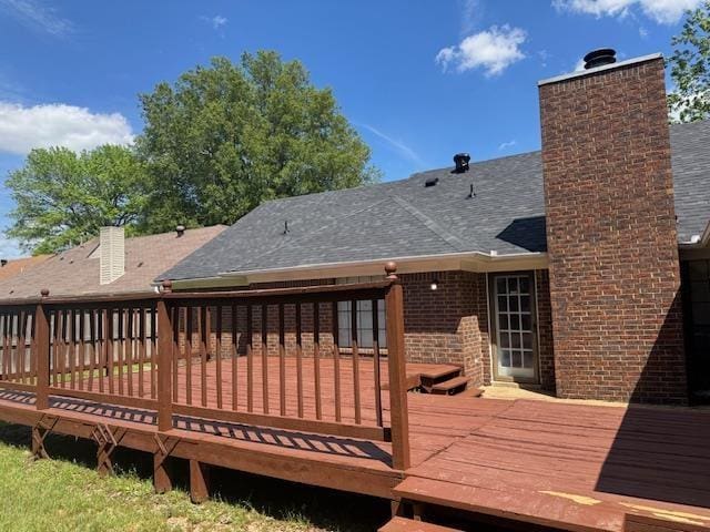 back of house with a deck, a chimney, a shingled roof, and brick siding