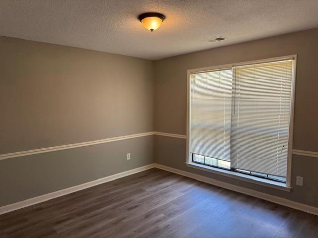 spare room with a textured ceiling, plenty of natural light, dark wood finished floors, and baseboards