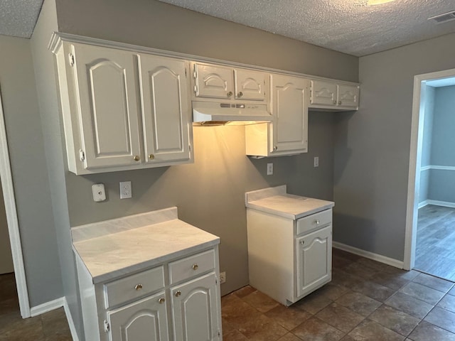 kitchen with white cabinets, a textured ceiling, under cabinet range hood, and light countertops