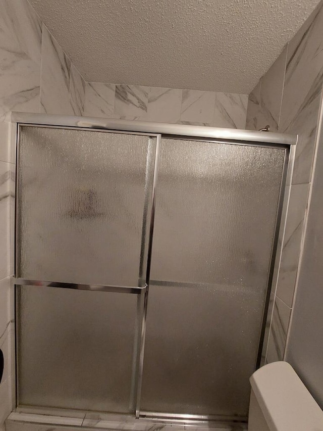 bathroom featuring a textured ceiling, toilet, and a stall shower
