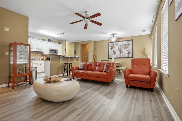living room with visible vents, ceiling fan, baseboards, and light wood-type flooring