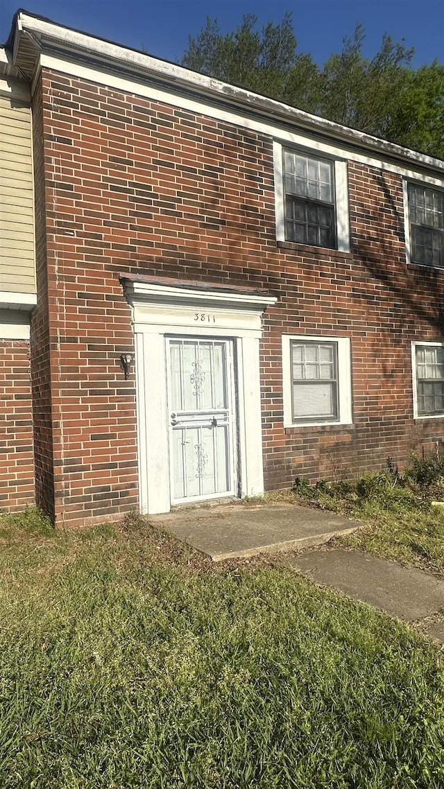 entrance to property featuring a yard and brick siding