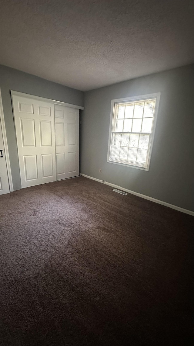 unfurnished bedroom with a closet, visible vents, dark carpet, baseboards, and a textured ceiling