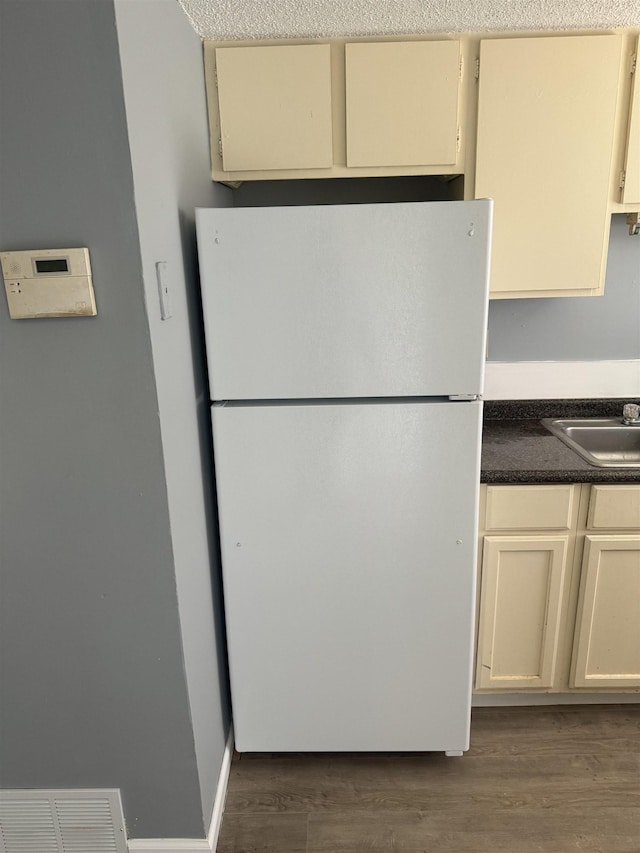 kitchen with freestanding refrigerator, dark countertops, a sink, visible vents, and cream cabinetry