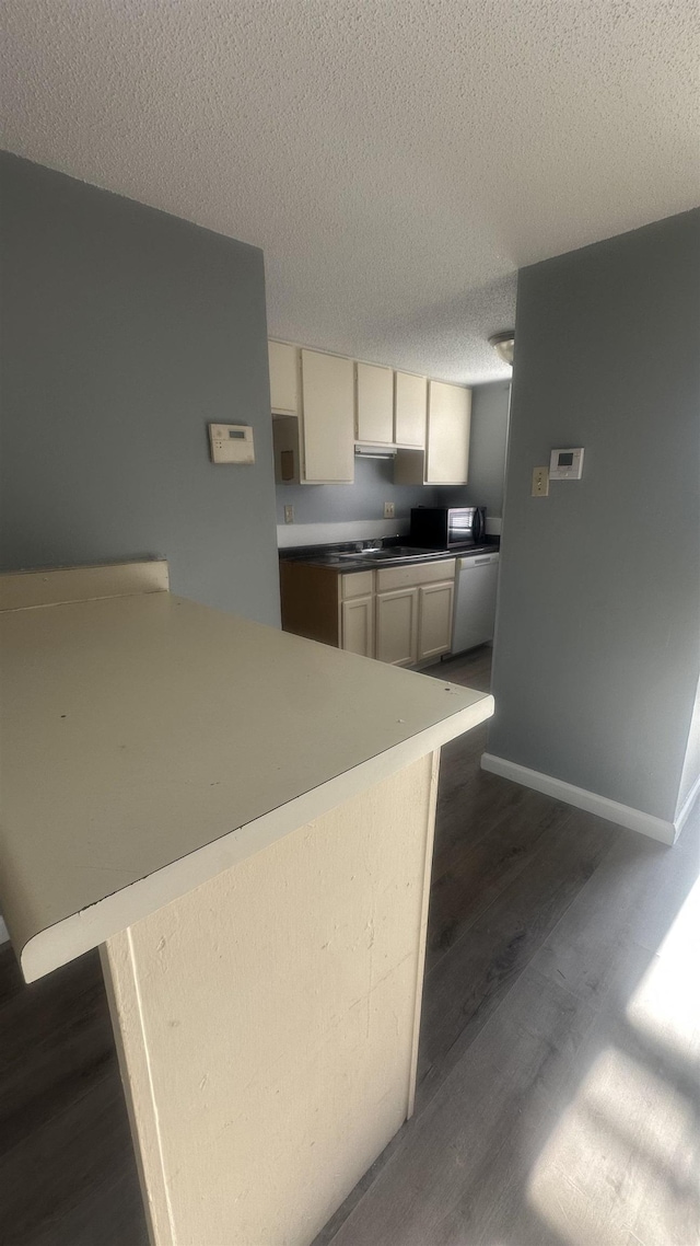 kitchen featuring a sink, dark wood-style flooring, white dishwasher, baseboards, and a textured ceiling