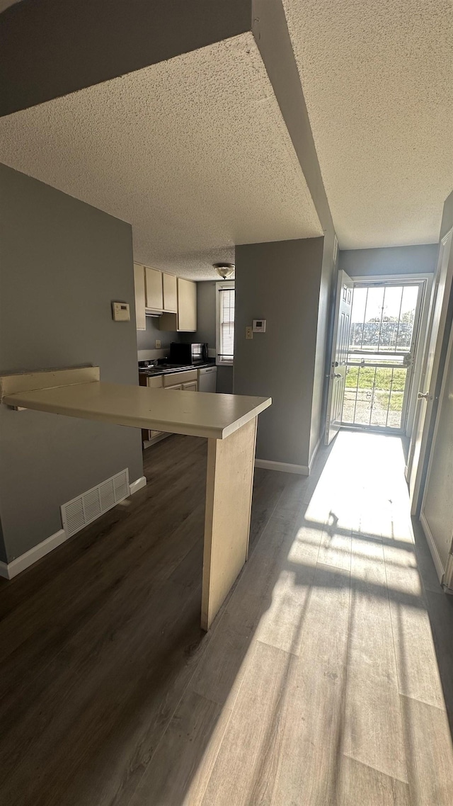 kitchen featuring a textured ceiling, visible vents, baseboards, open floor plan, and dark wood finished floors