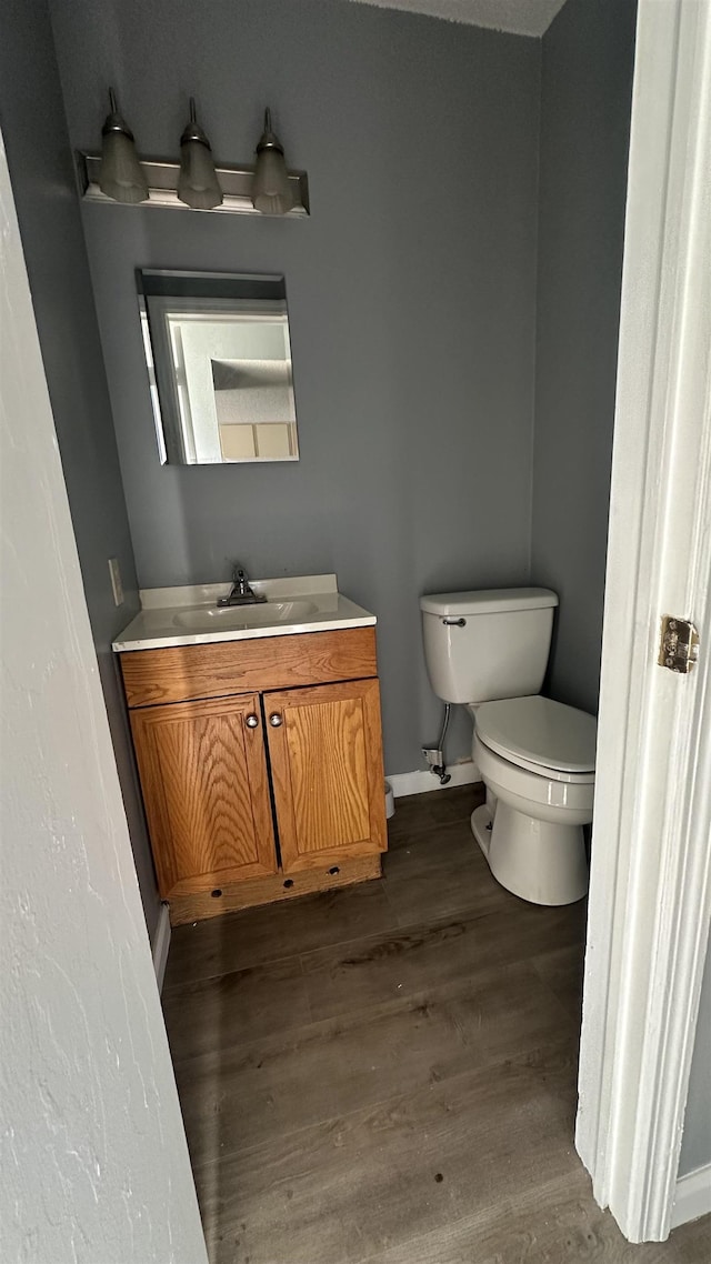 half bath featuring toilet, vanity, wood finished floors, and baseboards