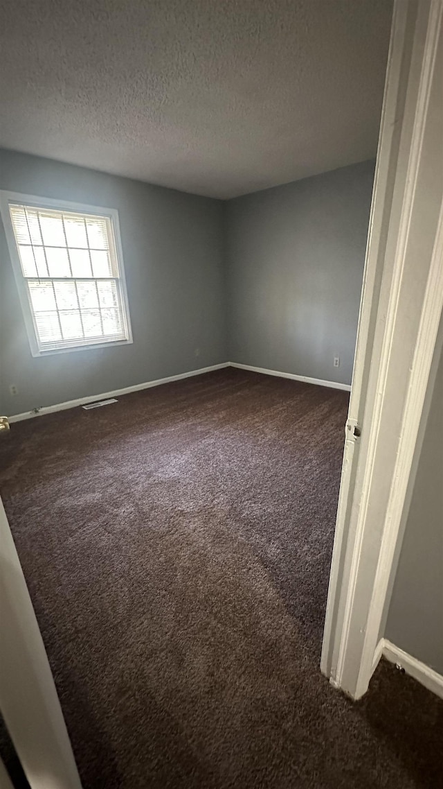 unfurnished room featuring baseboards and dark colored carpet