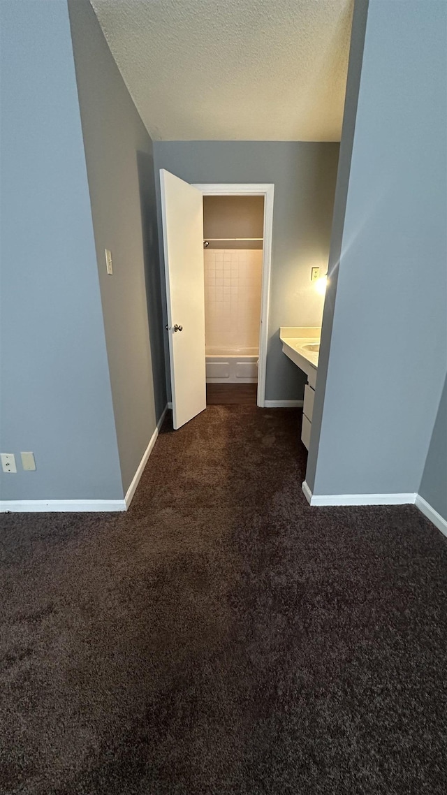 hall with dark carpet, a textured ceiling, and baseboards