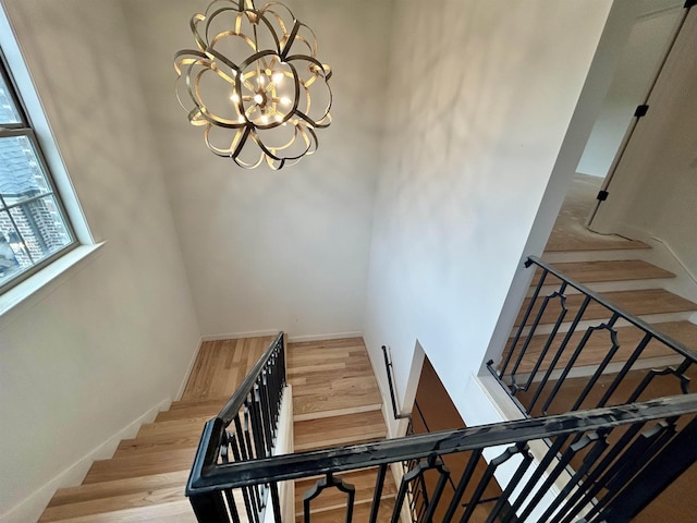 stairs with baseboards, wood finished floors, and a notable chandelier