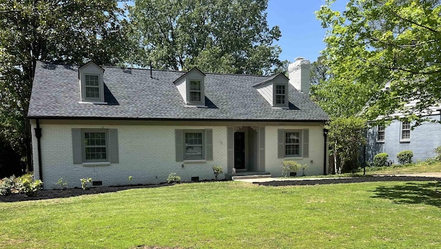 new england style home with brick siding, a front lawn, roof with shingles, a chimney, and crawl space